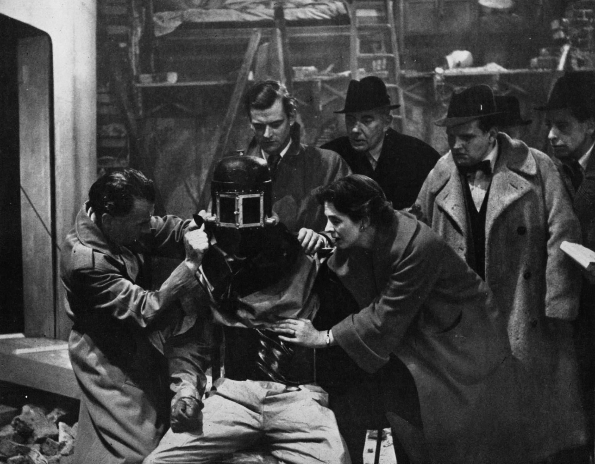 The cast struggle to remove a helmet from the first victim in Quatermass