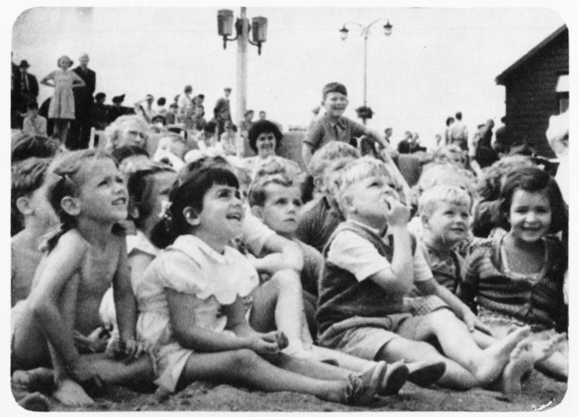 Children sit on the ground watching something off camera