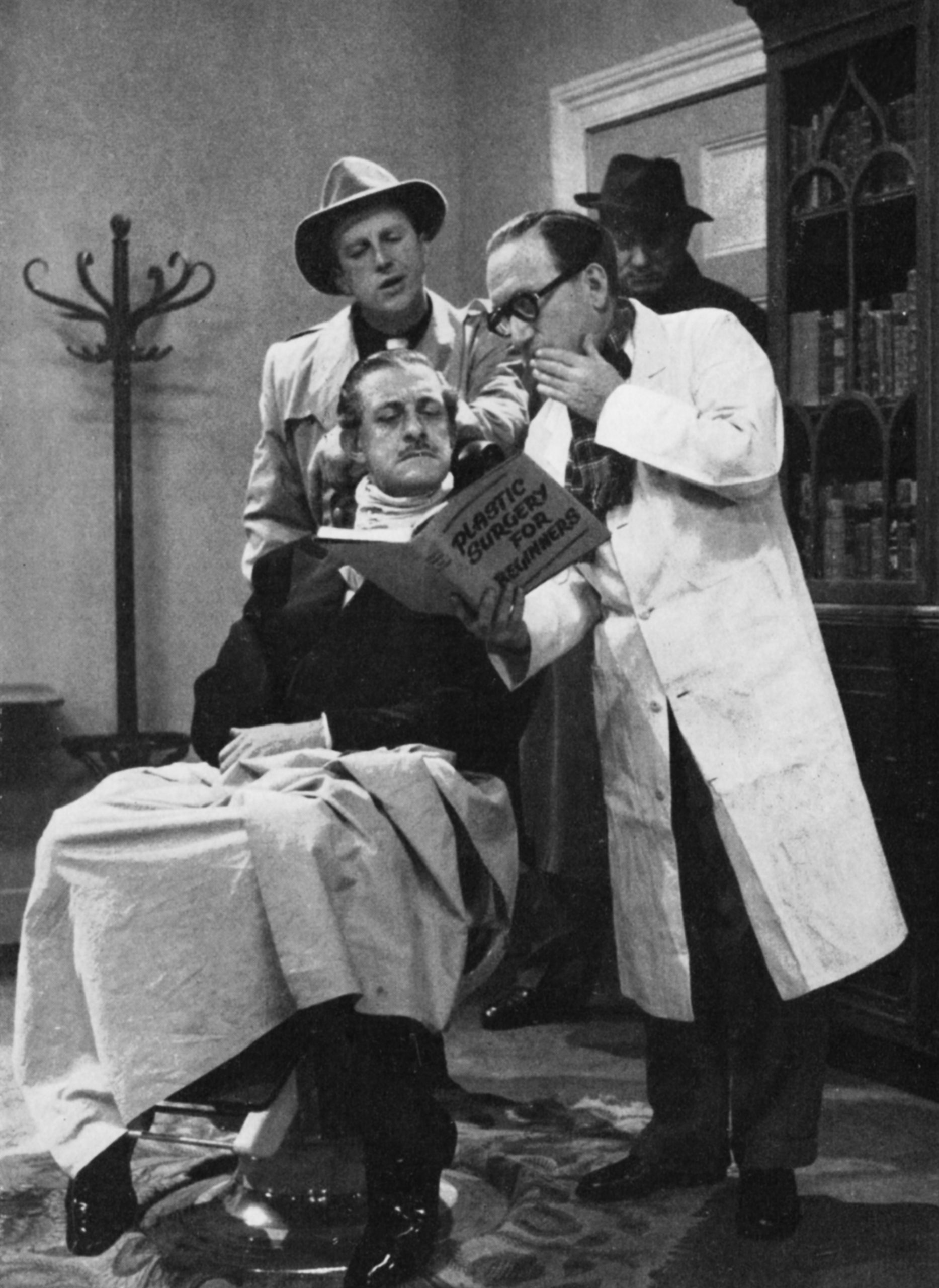 Leslie Mitchell in a doctor's chair with Arthur Askey looming over him with a book entitled "PLASTIC SURGERY FOR BEGINNERS"