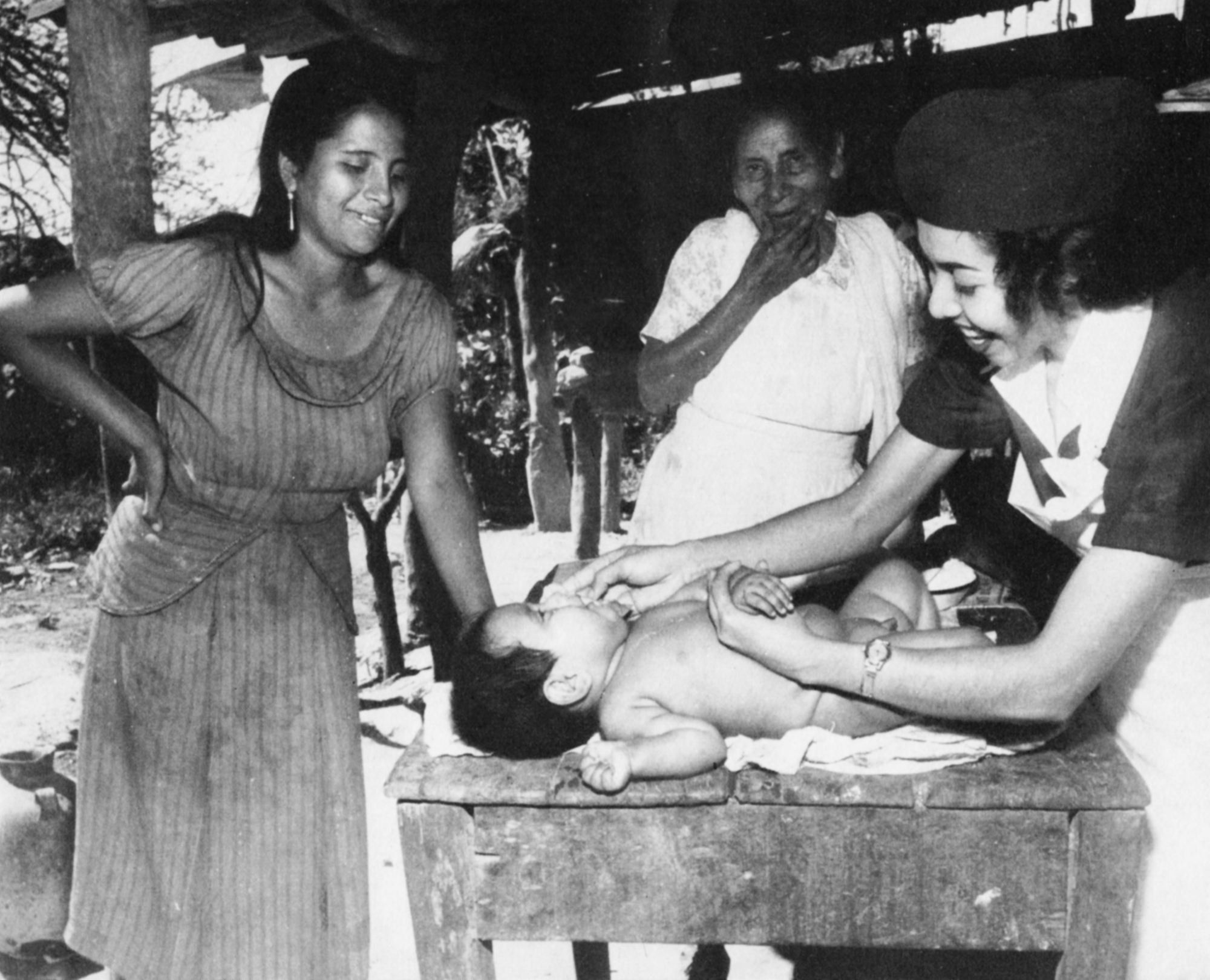A child is examined by a nurse as his mother stands over him