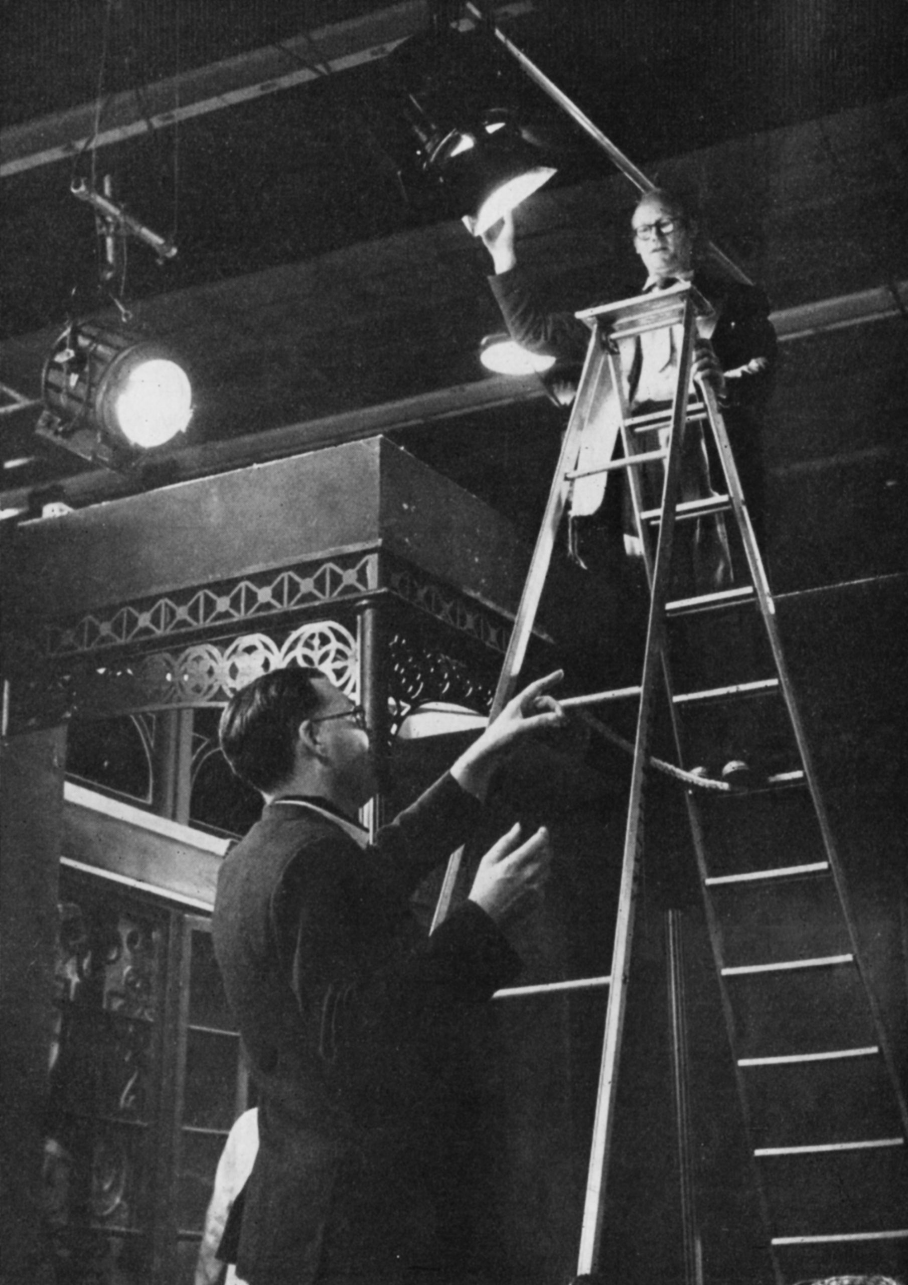 A man climbs a ladder to adjust a studio light.